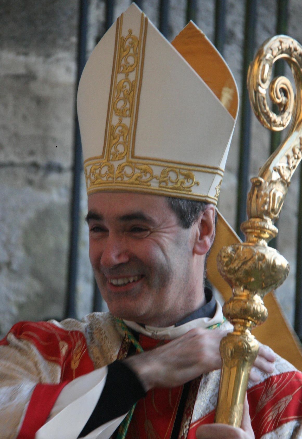 Personne en tenue religieuse, souriant avec une crosse dorée.